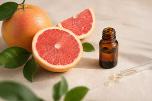 Egész és félbevágott rózsaszín grapefruitok barna illóolajos üveggel és pipettával