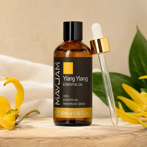 Ylang ylang illóolaj borostyánszínű 100 ml-es üvegben világos fa felületen, mellette arany színű kupakos üveg pipetta.