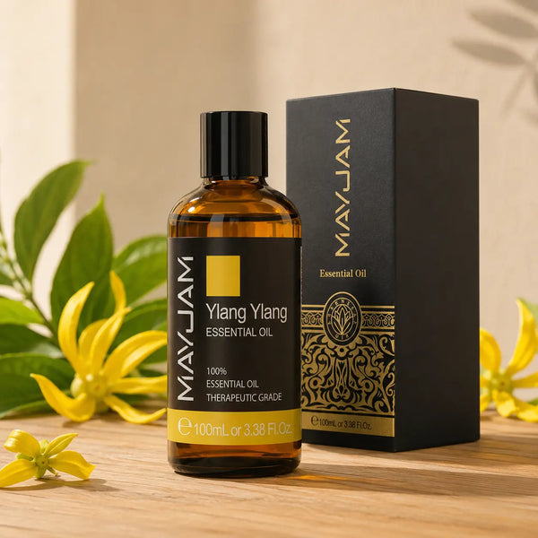 100 ml-es ylang ylang illóolaj borostyánszínű üvegben fekete prémium díszdoboz mellett, világos fa felületen.